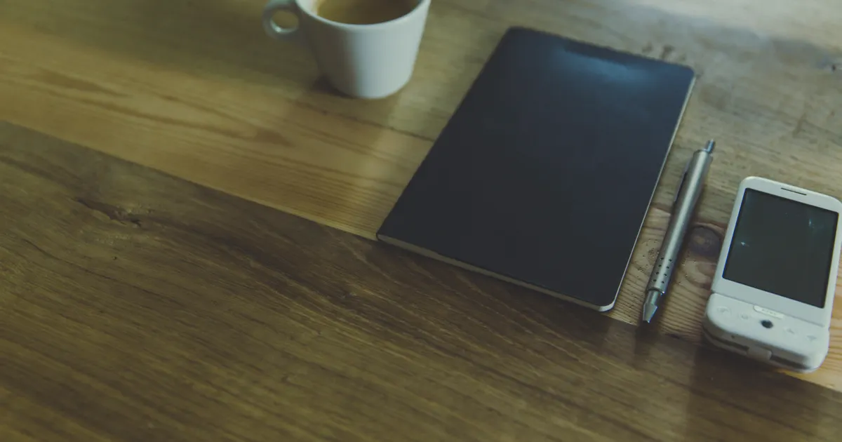 机の上に置かれたスマートフォンとコーヒー