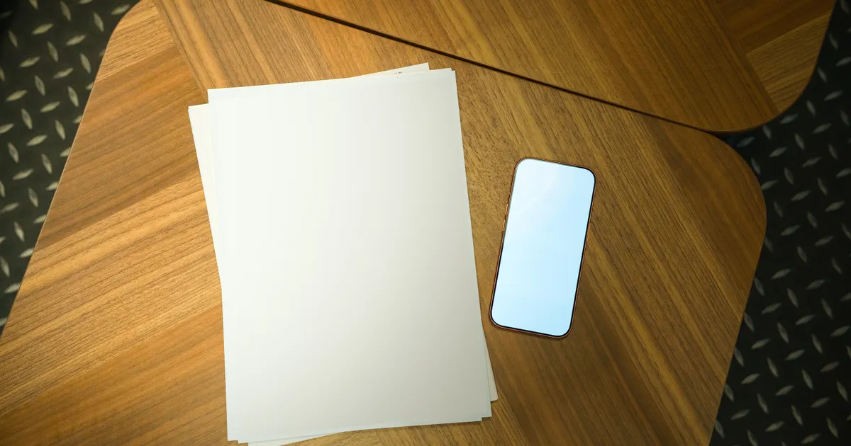 木の机に置かれた白い紙とスマートフォン